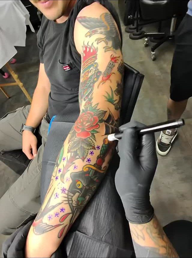 Full sleeve of American traditional tattoos on an arm being worked on by artist.