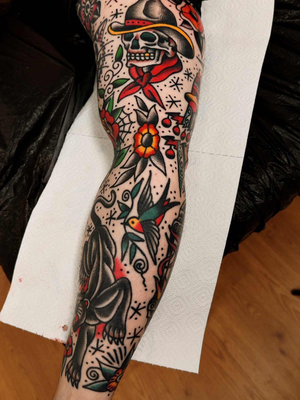 American traditional tattoo sleeve on an arm featuring a skull, panther, and swallow.