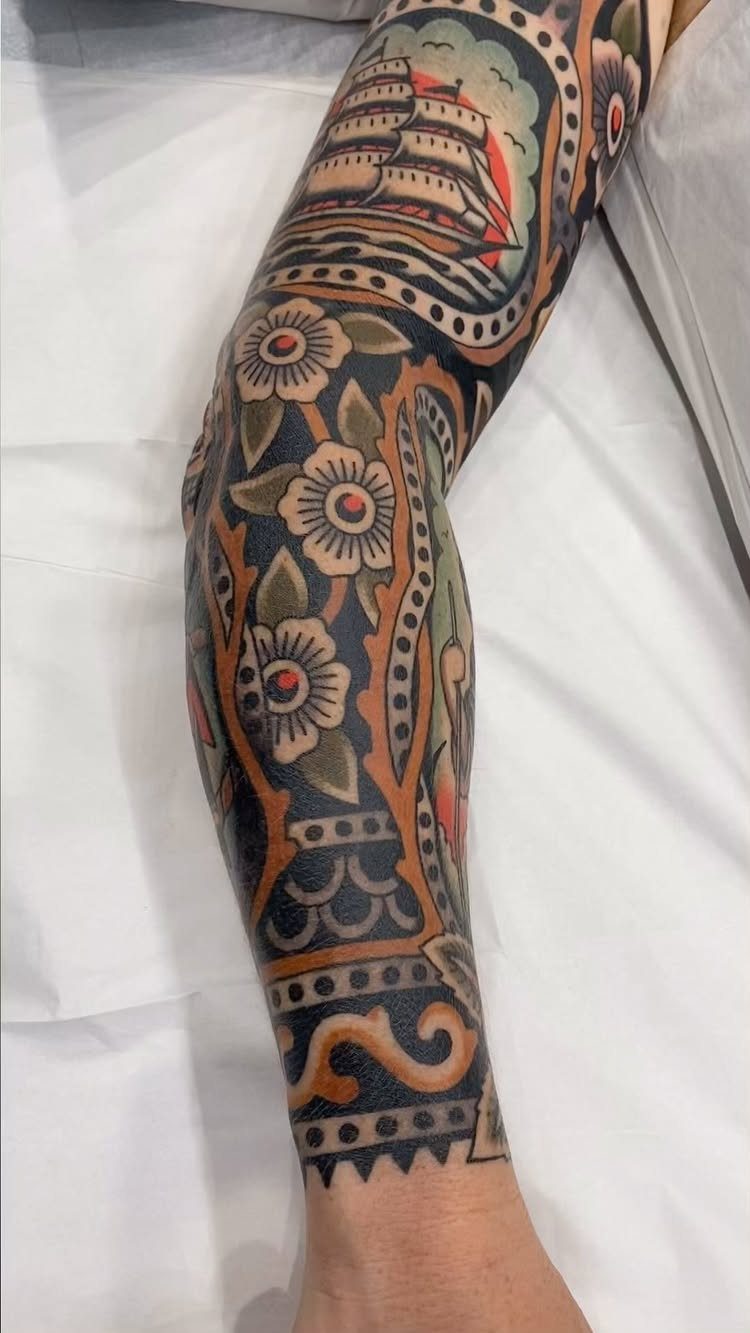 American traditional sleeve tattoo featuring a sailing ship and floral patterns on an arm.