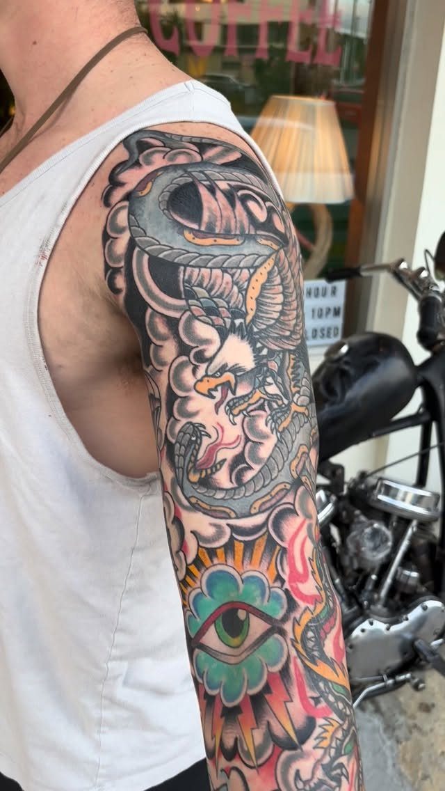 American traditional tattoo sleeve on an arm featuring an eagle, snake, and eye.