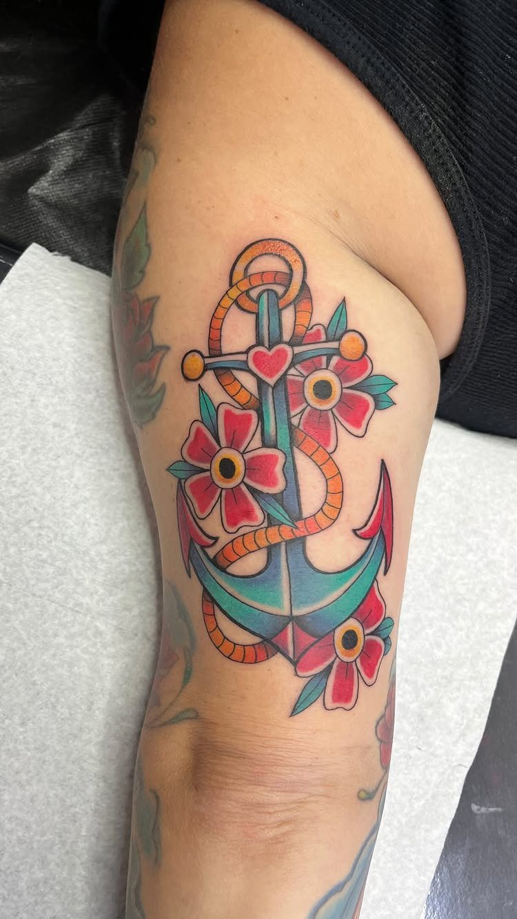Teal anchor tattoo with gold rope and red flowers on a person's arm.