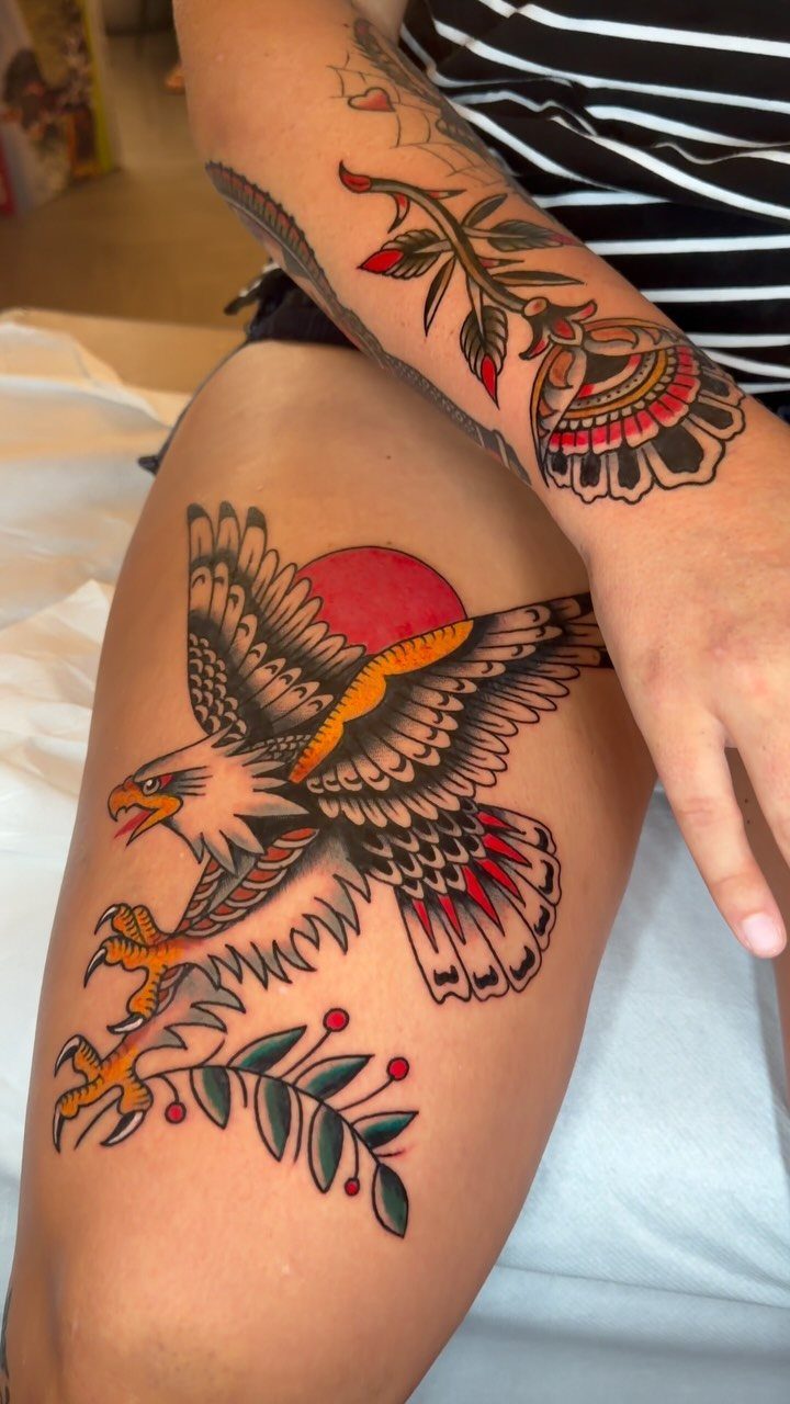 Bald eagle tattoo on a thigh with a red sun and olive branch.