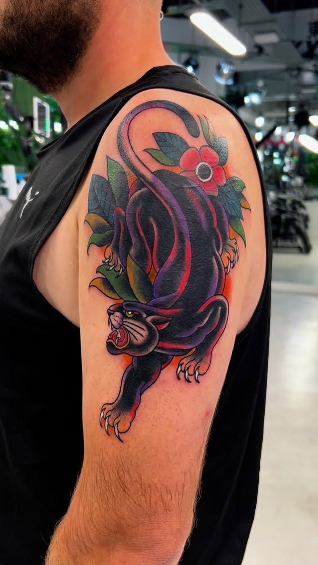 Black panther tattoo with red accents and floral elements on a man's arm.