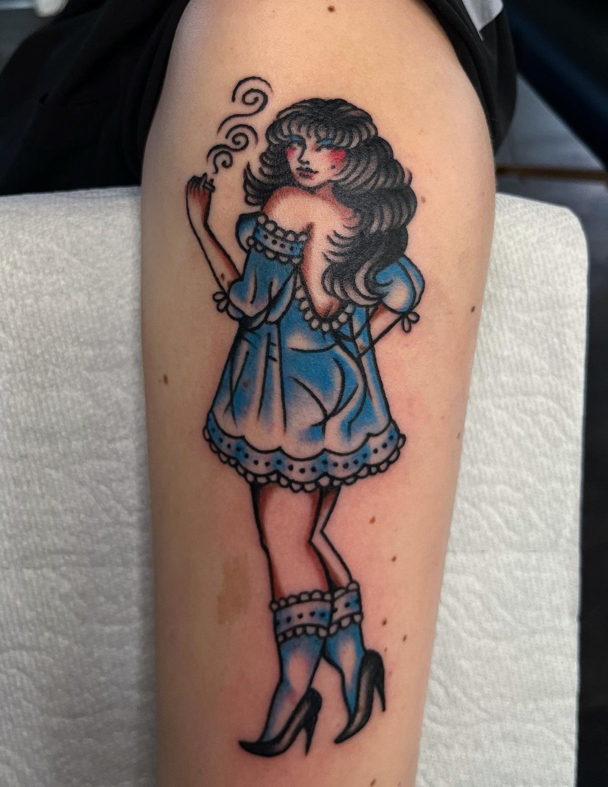 Pinup girl tattoo with blue dress and dark hair on a person's leg.