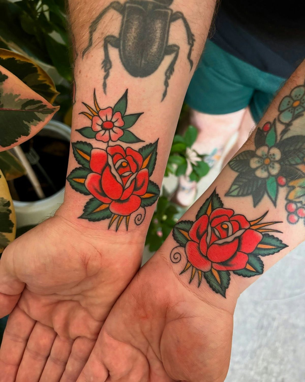 Red rose tattoos with green leaves on two people's wrists in traditional style.