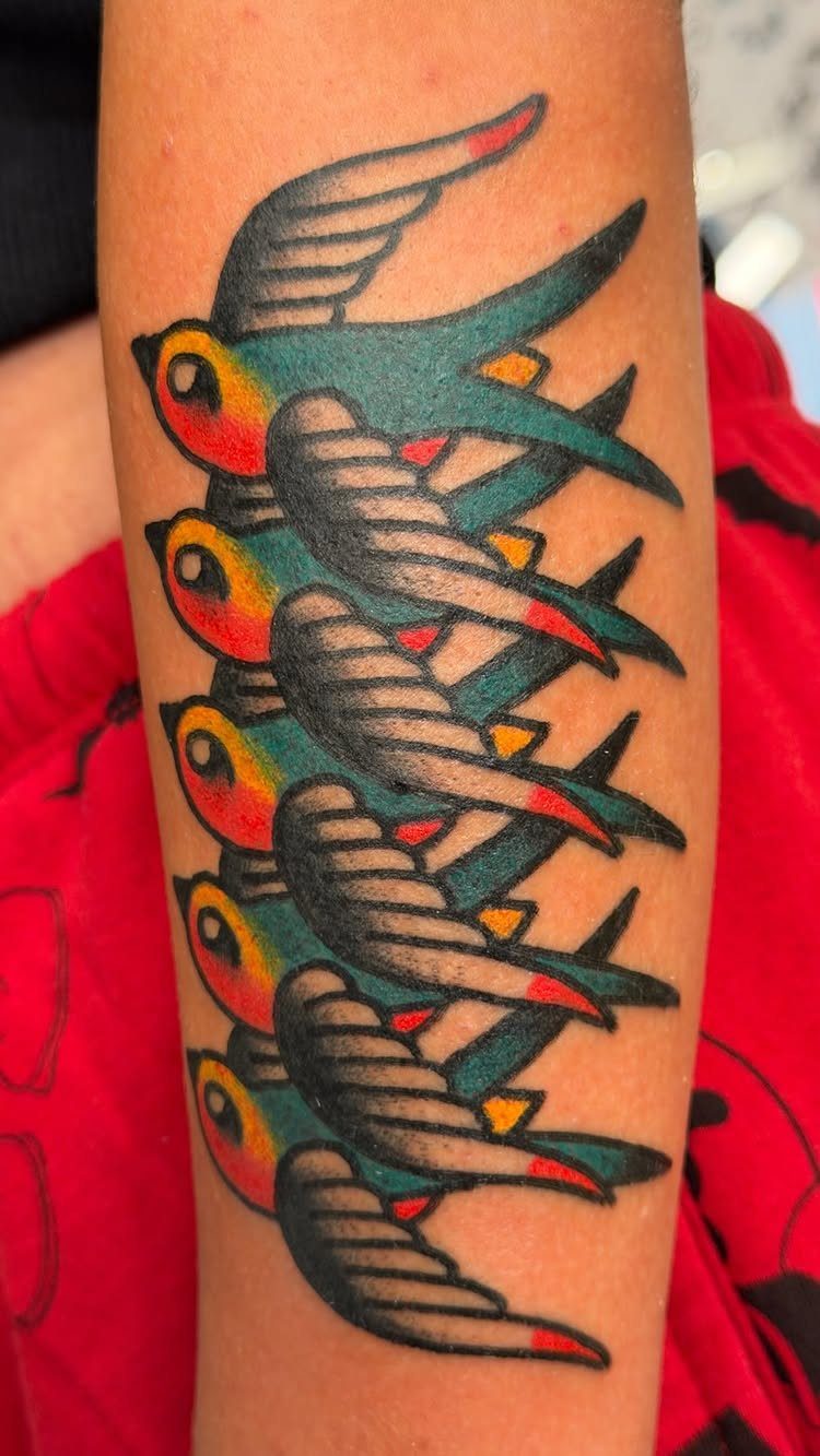 Five traditional swallow tattoos with red and teal colors on a person's arm.