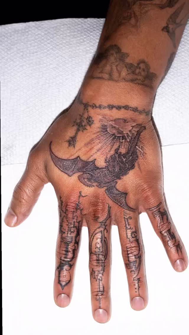 Tattooed hand featuring a winged angel figure and detailed finger ink designs.