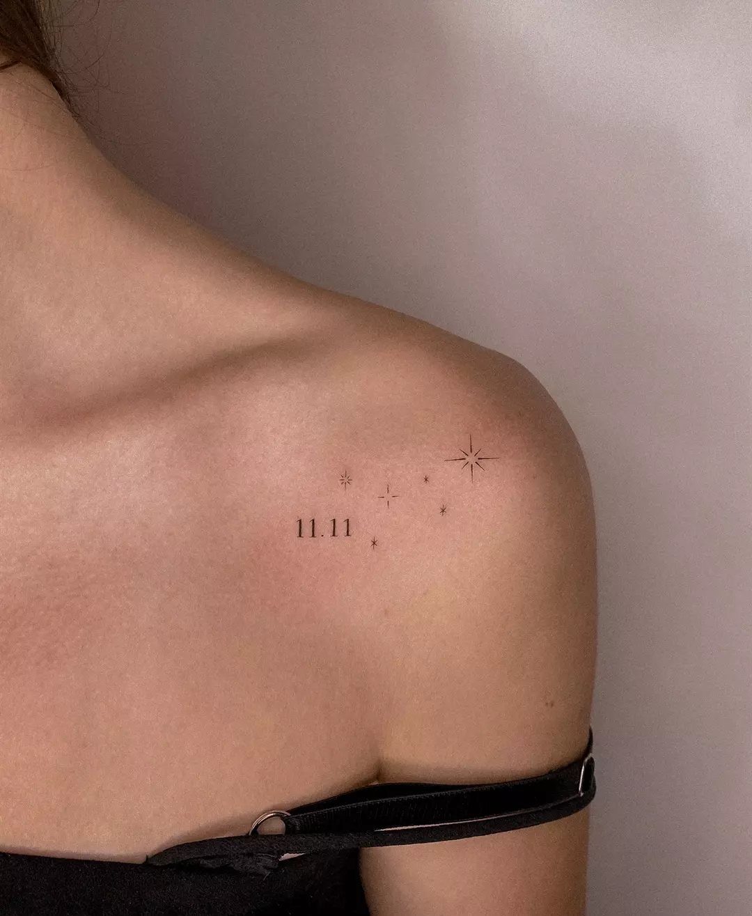 Minimalist 11.11 tattoo with small stars on a person's shoulder