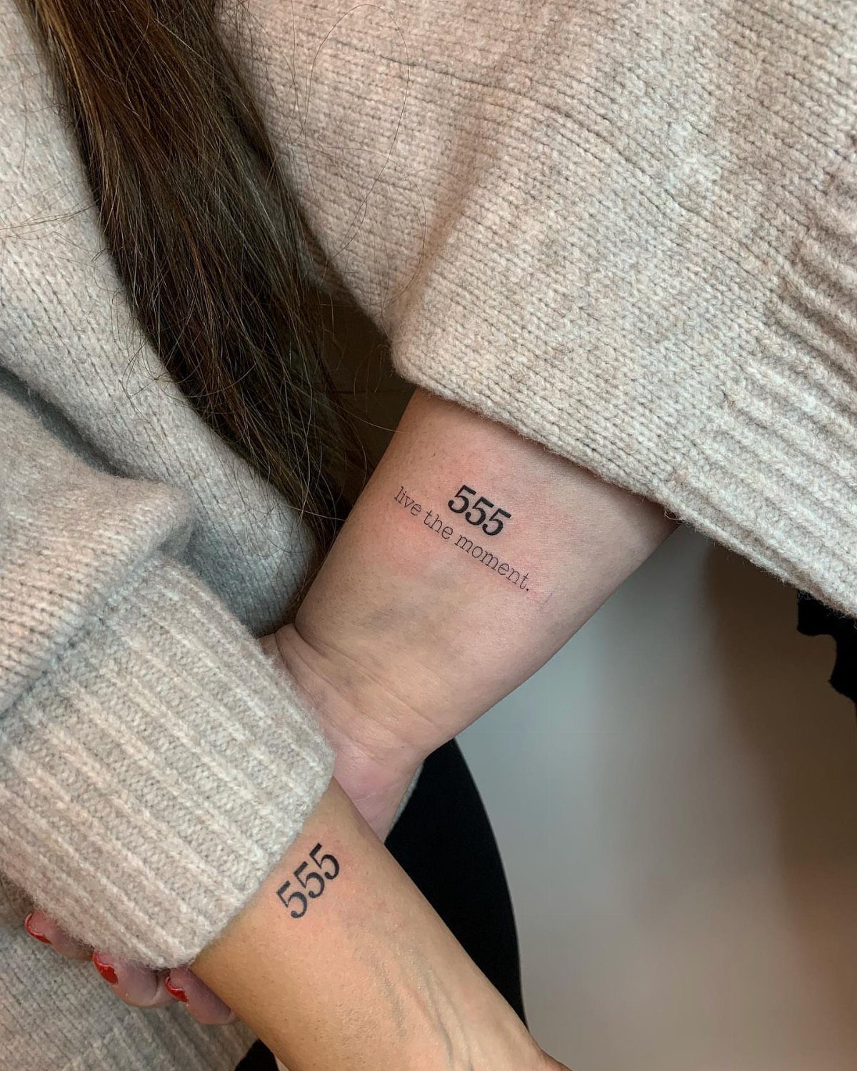 Two wrists with small black tattoos of the angel number 555