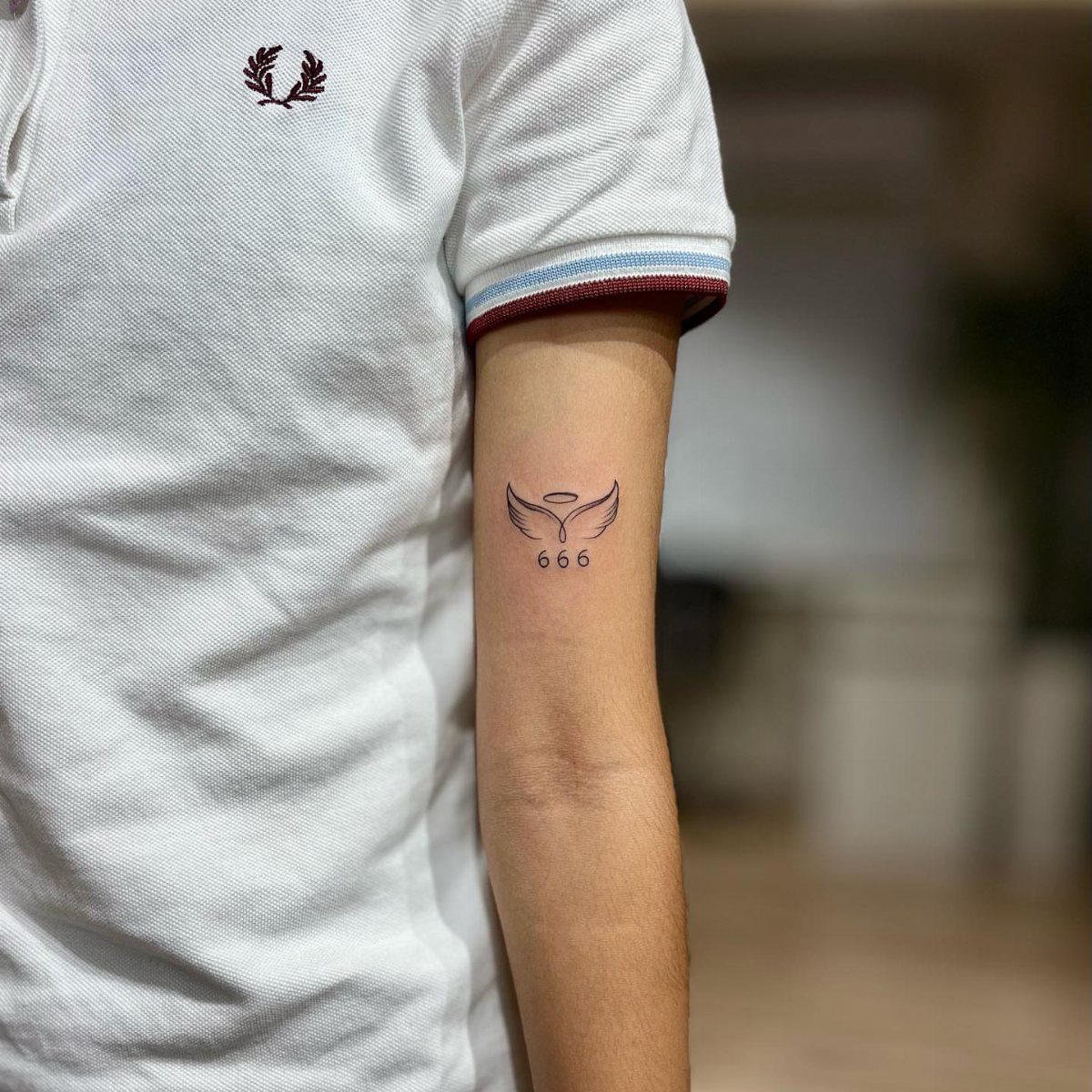 Small black tattoo of 666 with wings and halo on an upper arm