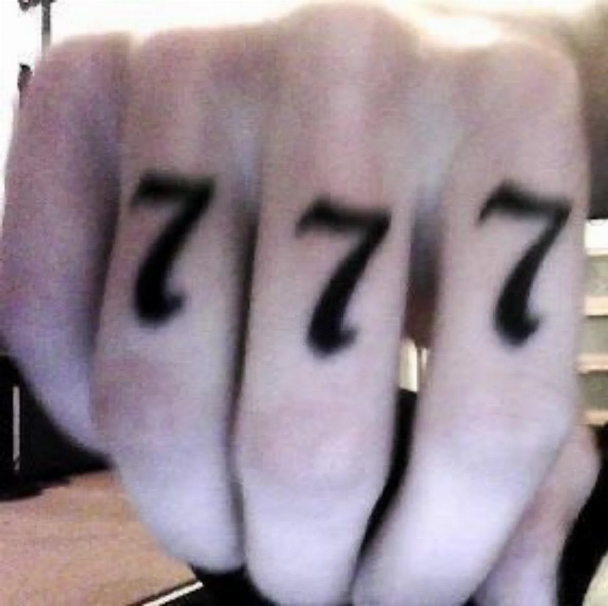 Three black number 7 tattoos on the fingers of a person's hand.