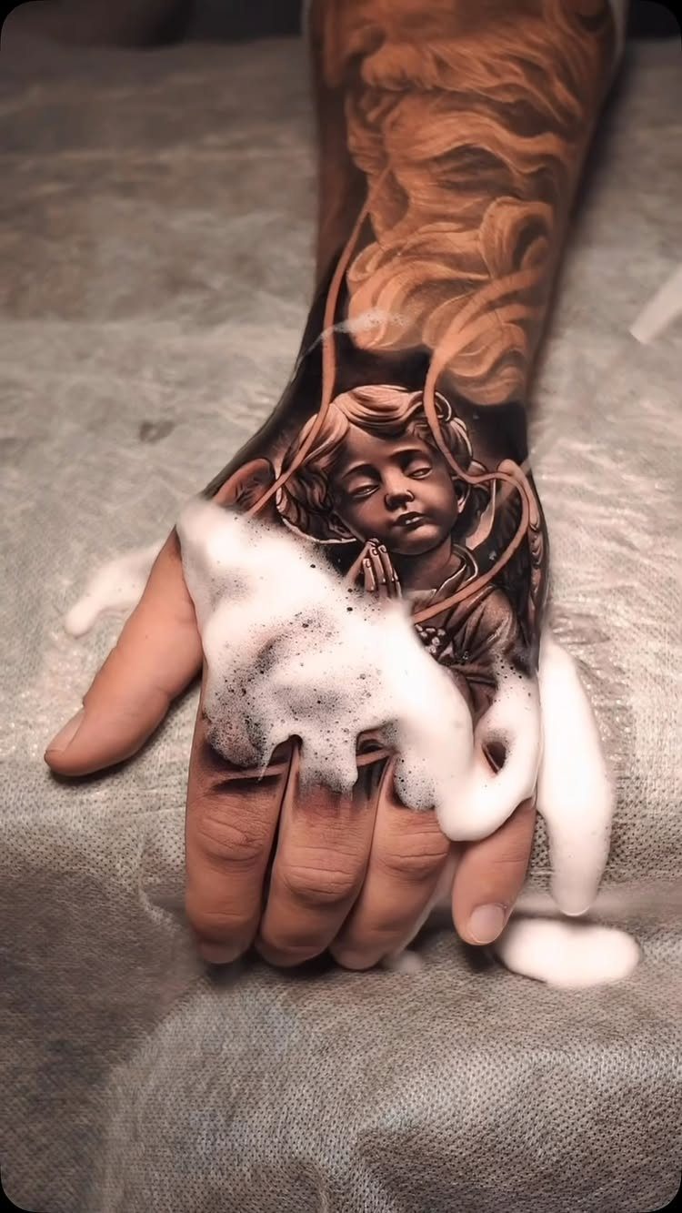 Detailed black and grey angel tattoo on a hand covered in soap foam