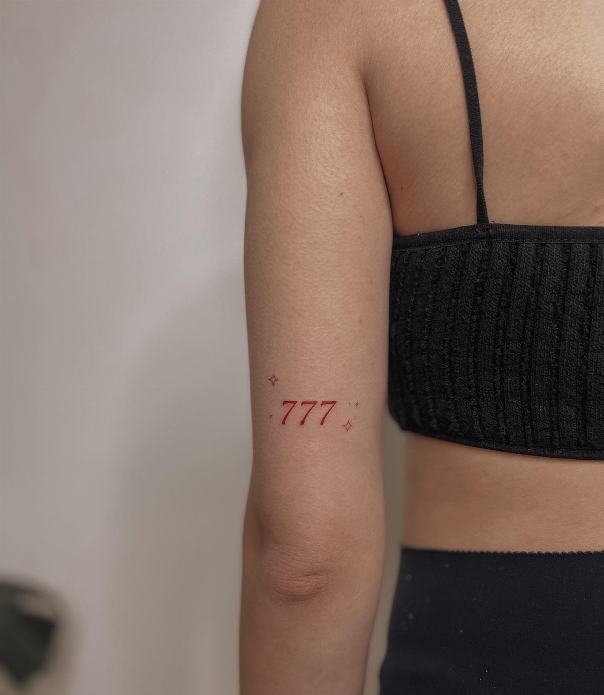 Red 777 angel number tattoo with small stars on a person's upper arm
