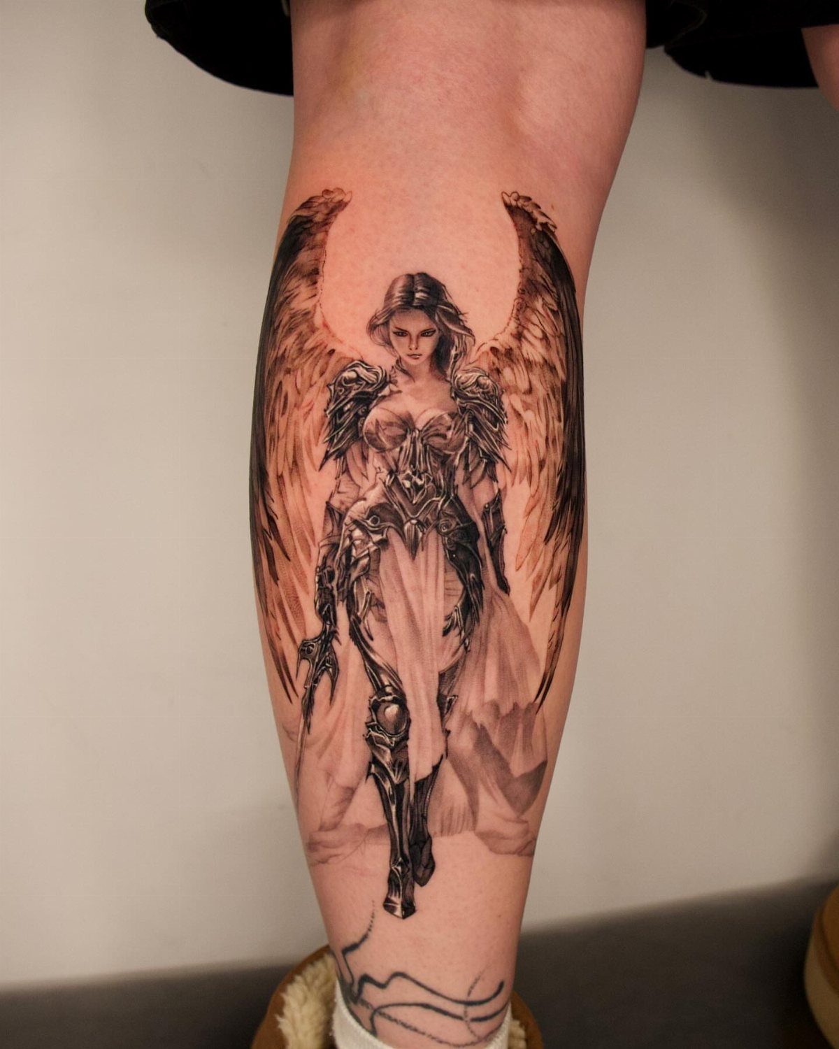 Female angel warrior tattoo in armor with wings on a person's lower leg