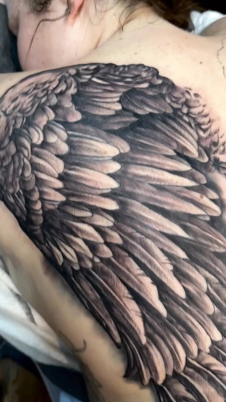 Detailed black and grey angel wing tattoo covering a person's upper back.