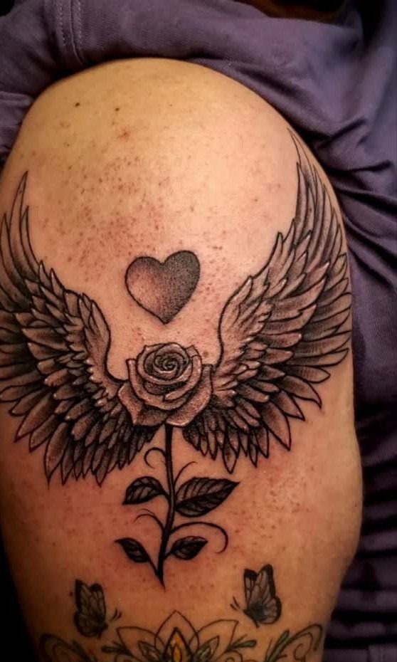 Tattoo on an arm showing angel wings, a heart, and a rose.