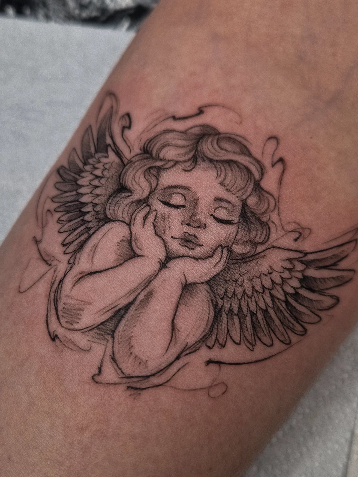 Cherub tattoo with curly hair and wings on a person's skin.
