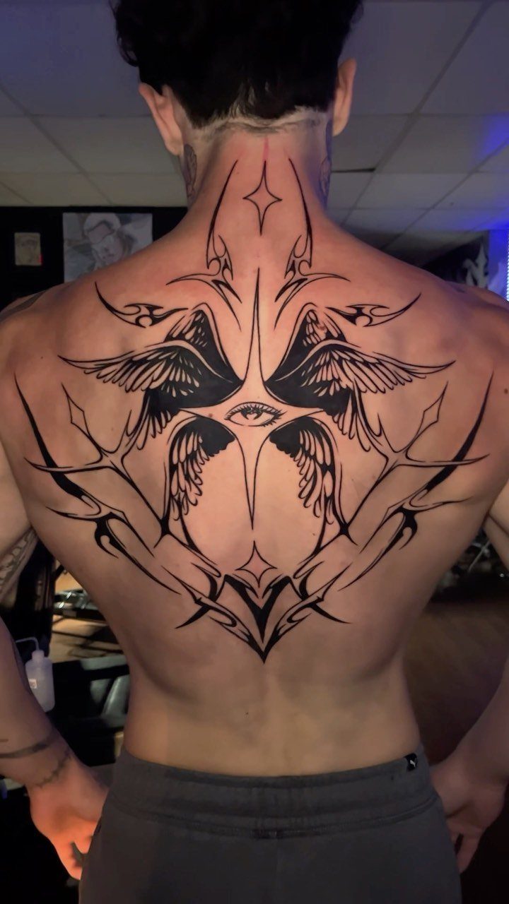 Large tribal angel wing tattoo with a central eye on a man's back