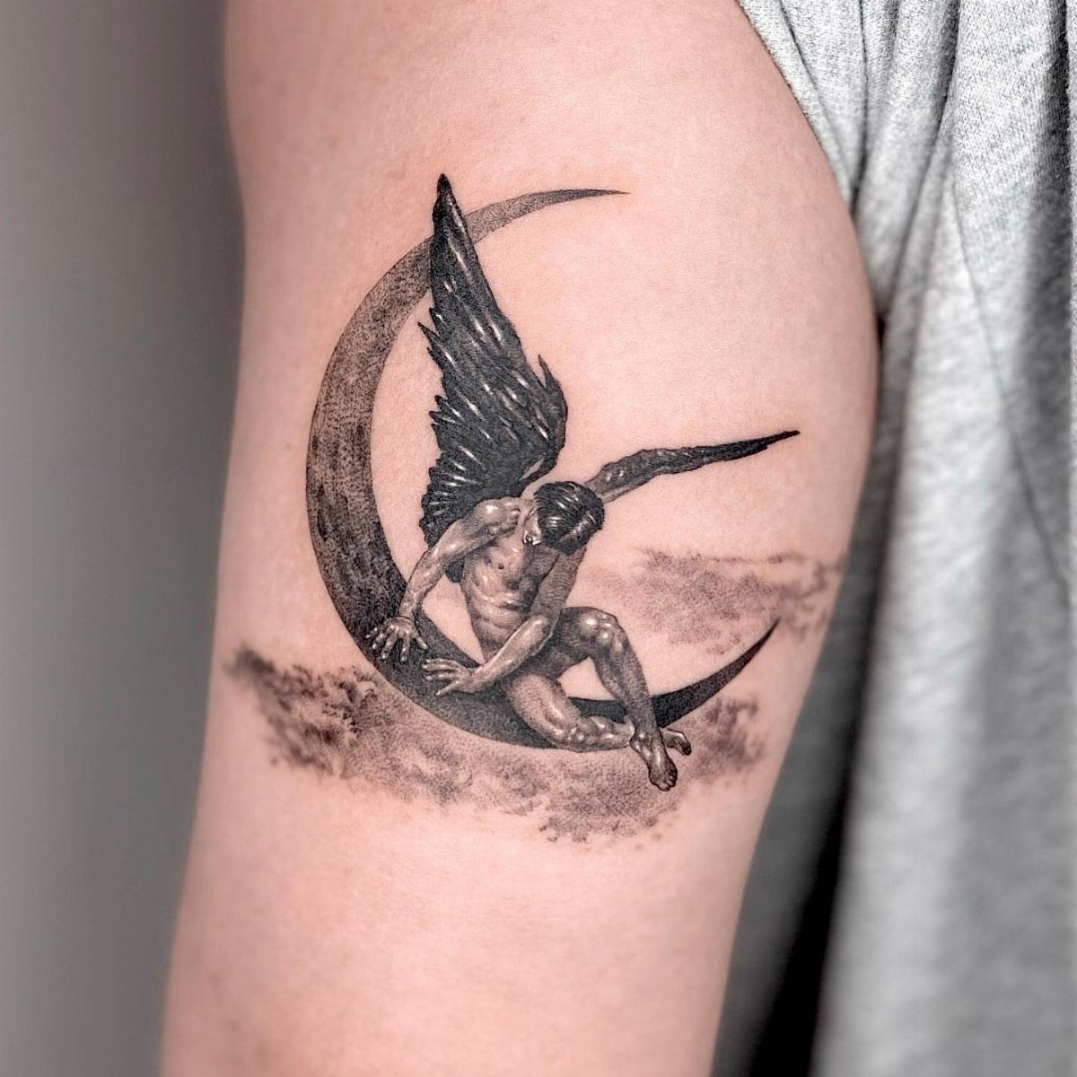 Winged angel tattoo sitting on a crescent moon with shaded clouds on arm