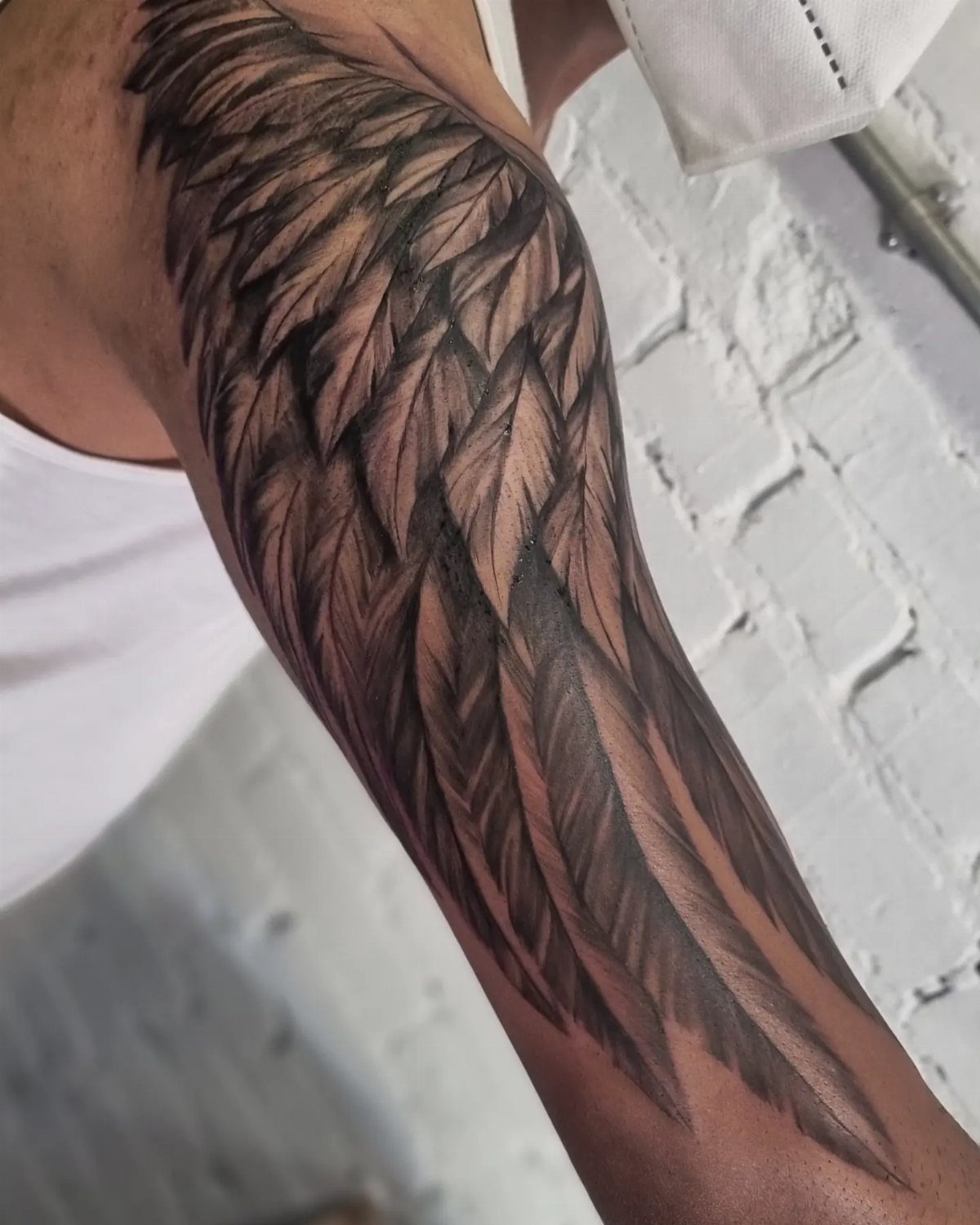 Detailed black and grey angel wing tattoo on a person's upper arm