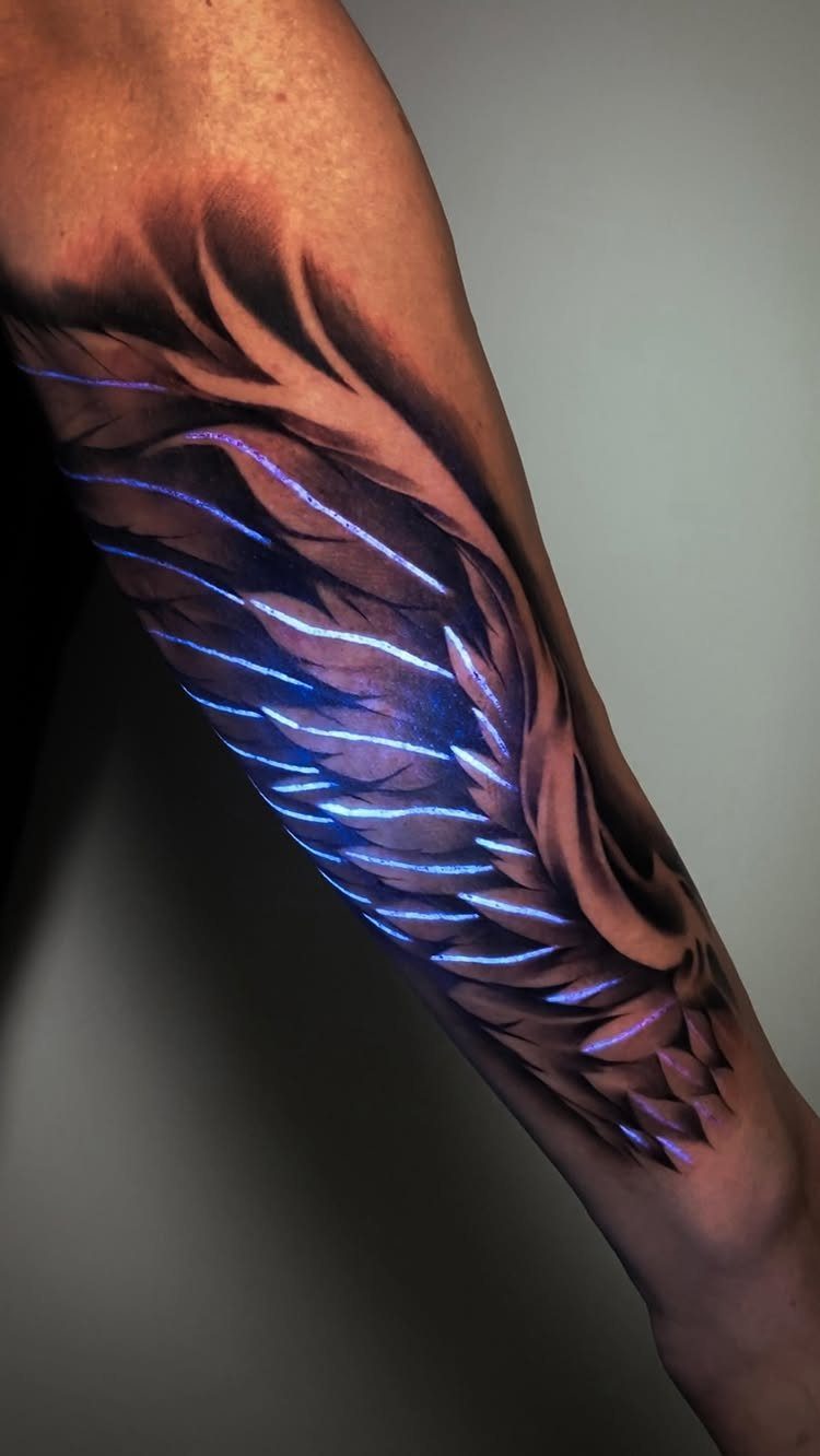 Angel wing tattoo on an arm with glowing blue highlights and grey shading