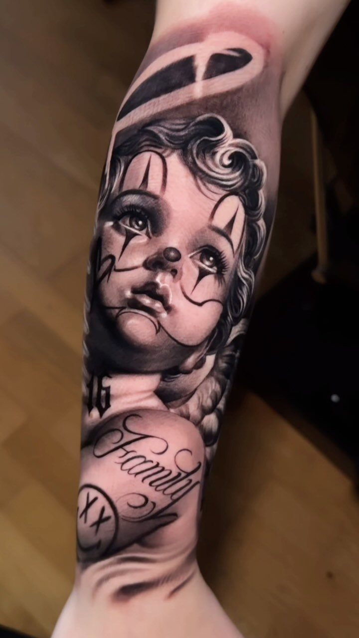 Cherub tattoo with clown makeup and a halo on a person's forearm