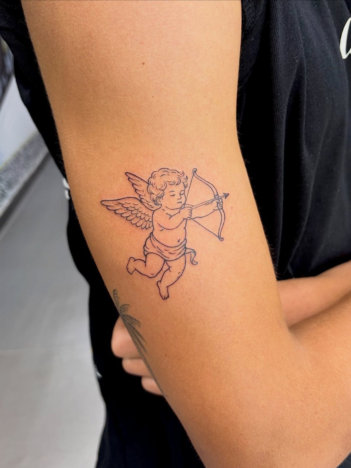 Cupid angel tattoo with bow and arrow on a person's upper arm