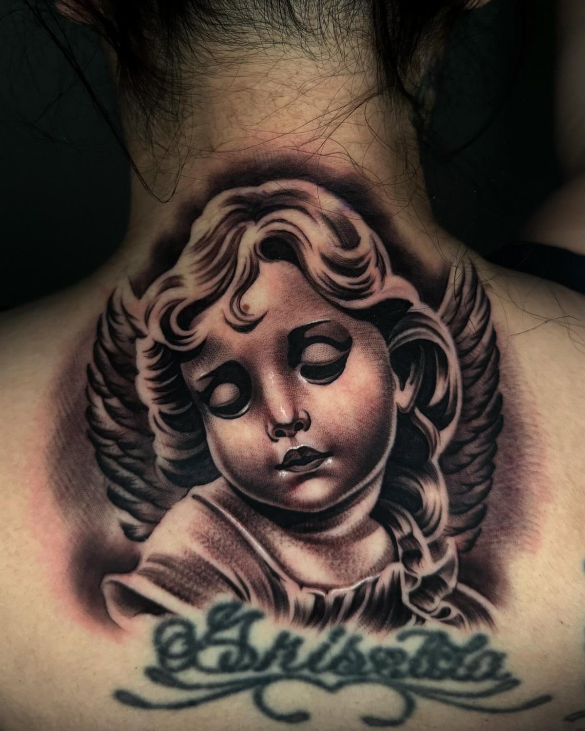 Baby angel tattoo on the upper back and neck with cursive name below.