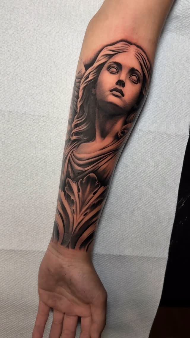 Realistic black and grey angel statue tattoo on a person's forearm