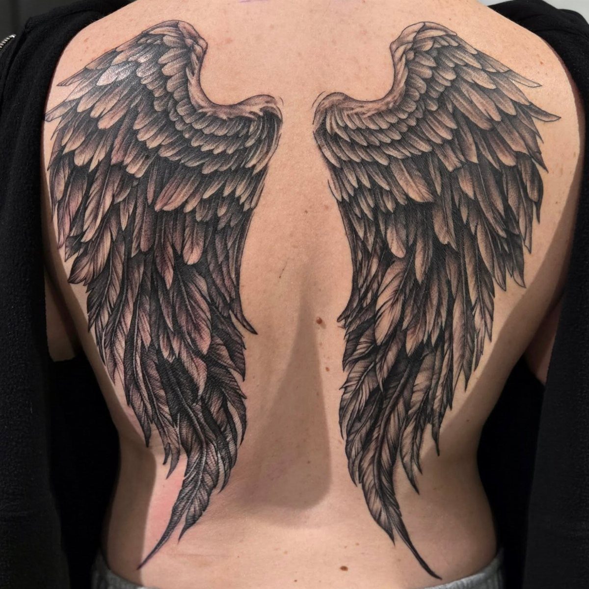 Large black and grey angel wings tattoo covering a person's entire back.