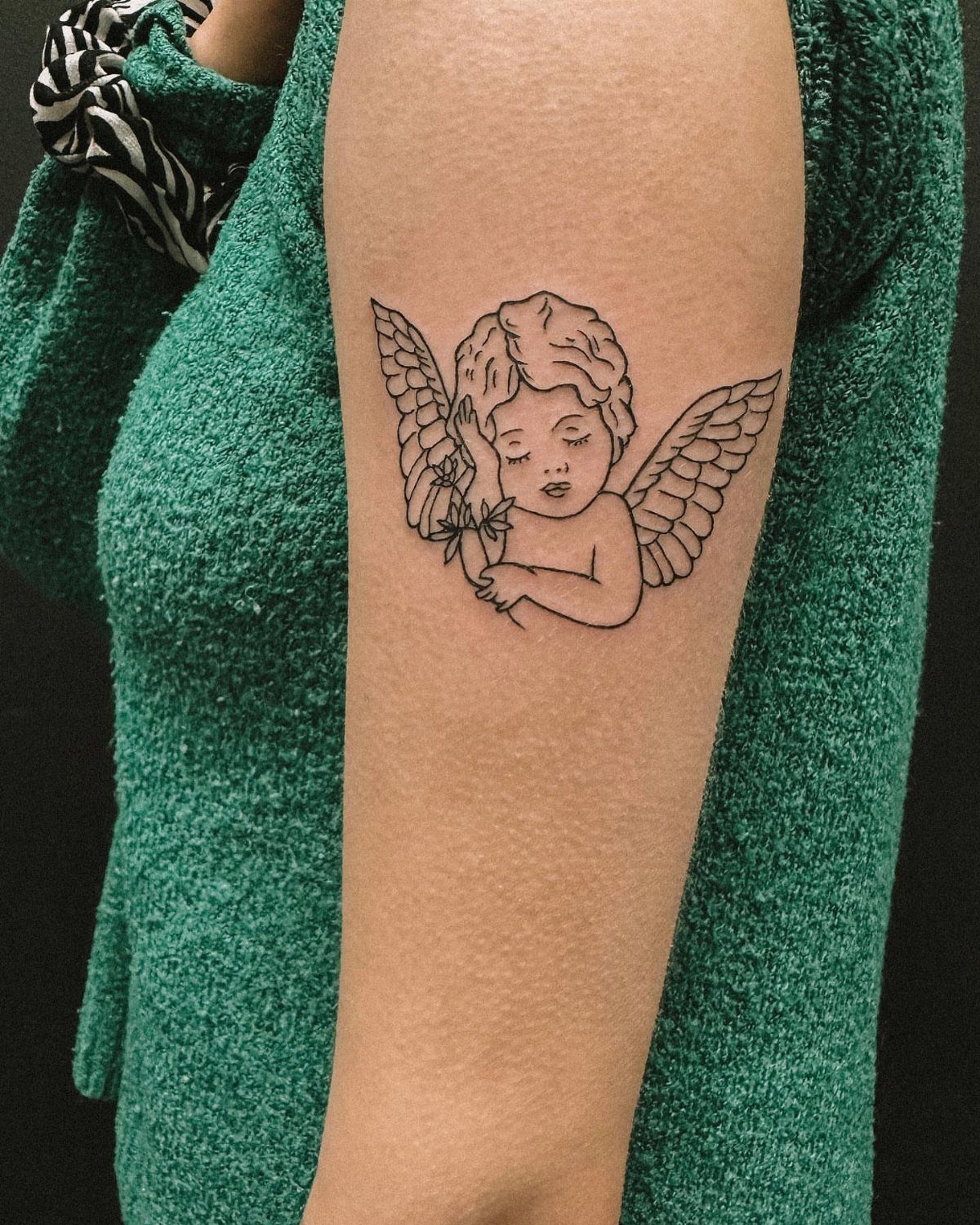 Angel tattoo with wings on a person's upper arm wearing green clothing