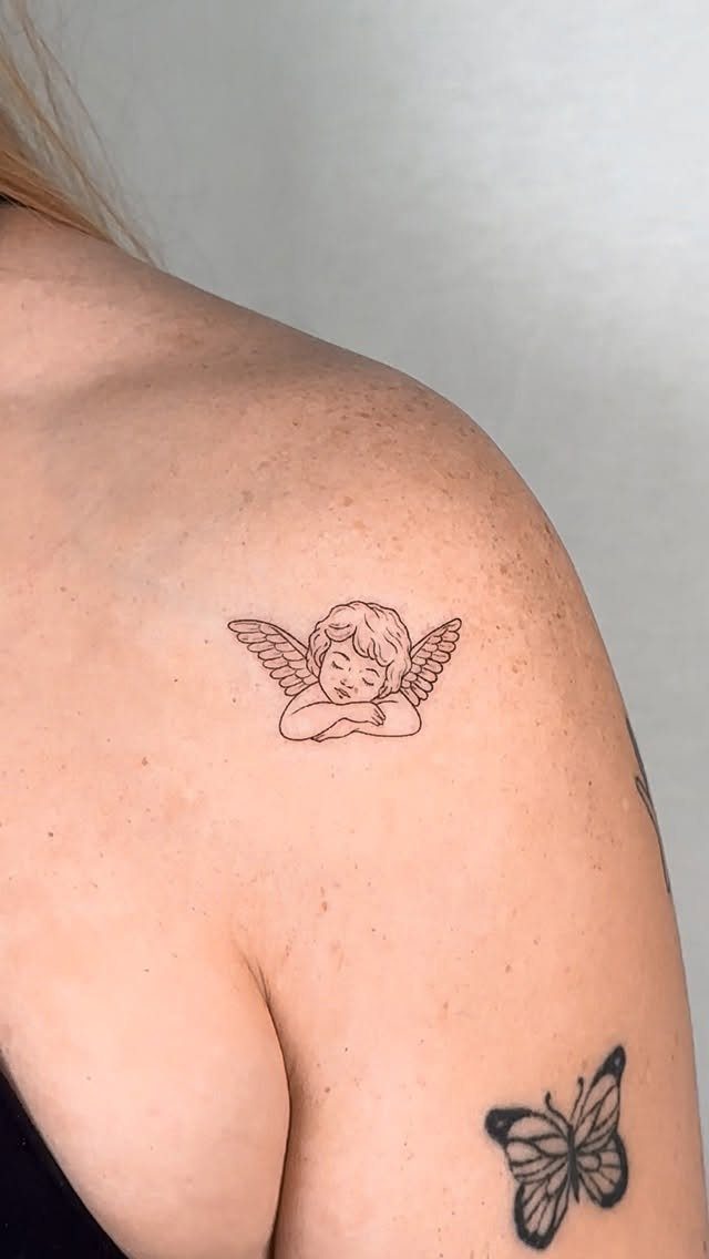 Sleeping angel tattoo with wings on a woman's shoulder and a butterfly tattoo.