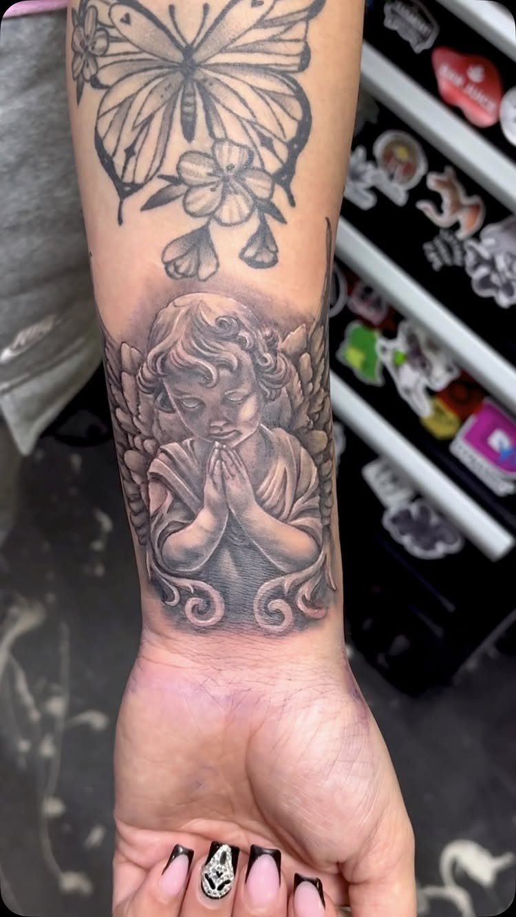 Praying cherub tattoo on a wrist with a butterfly tattoo above it