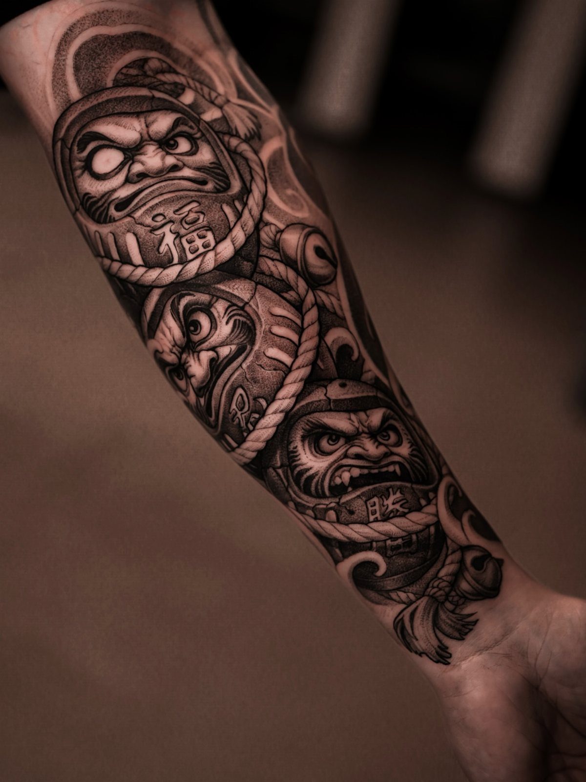 Three Daruma doll tattoos on a forearm with traditional Japanese cloud patterns