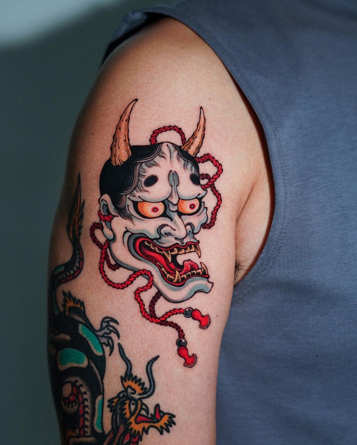 Hannya mask tattoo with red cords on a person's upper arm