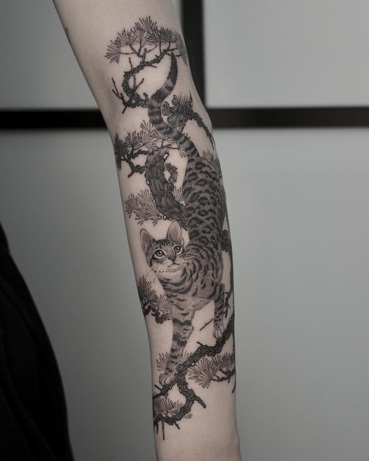 Tabby cat climbing a pine tree tattoo on a person's forearm