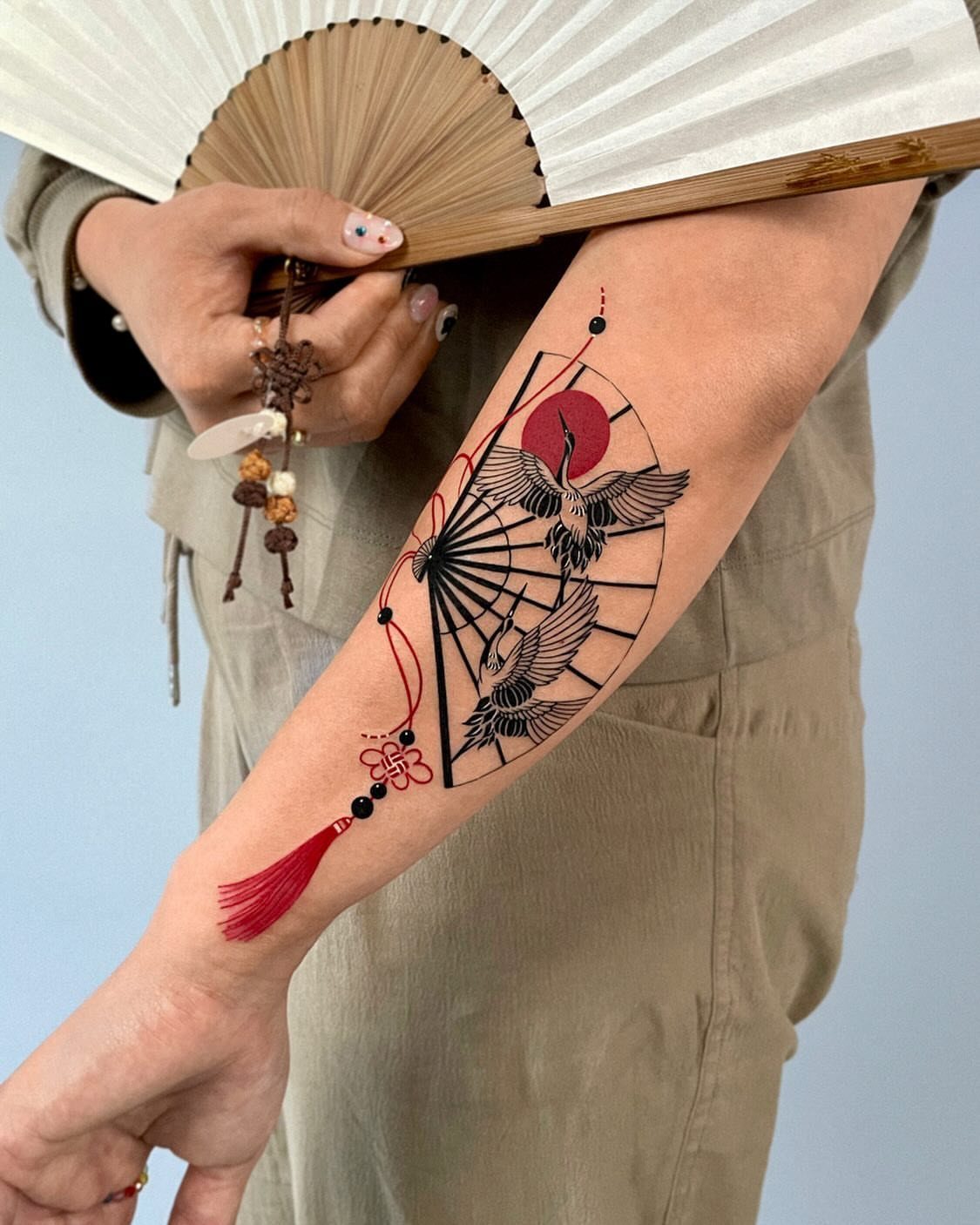 Japanese crane tattoo on a forearm with a red sun and fan design
