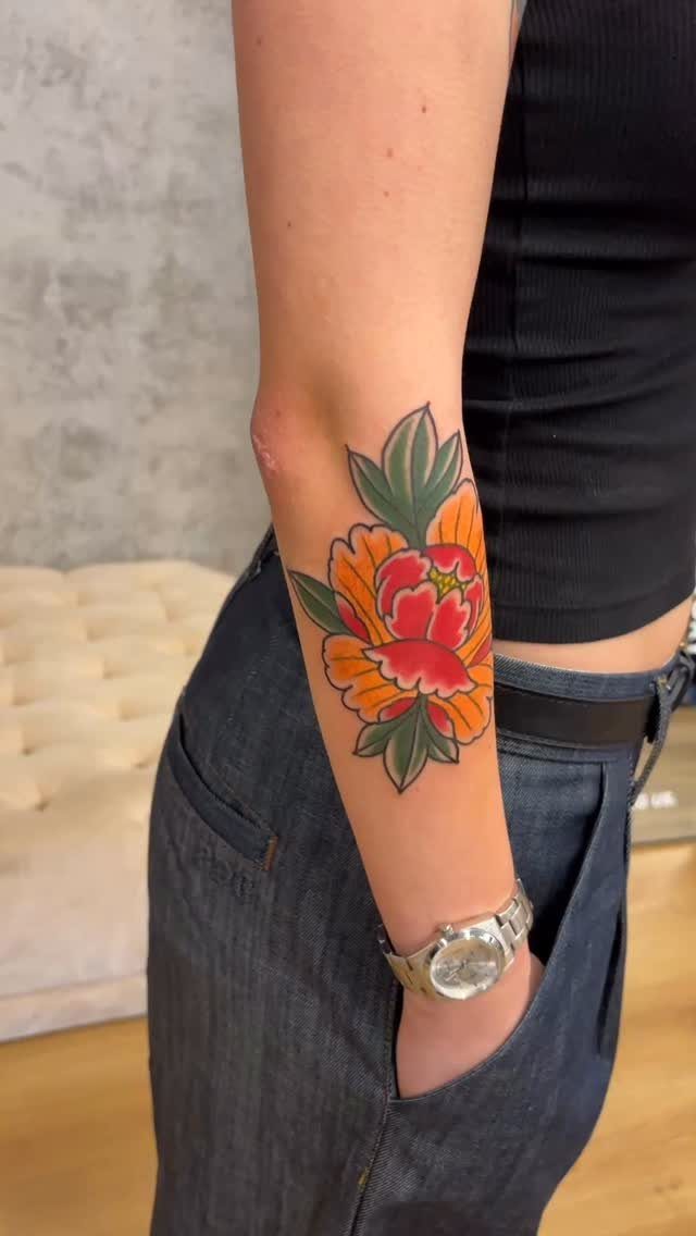Japanese flower tattoo on a forearm with orange petals and green leaves