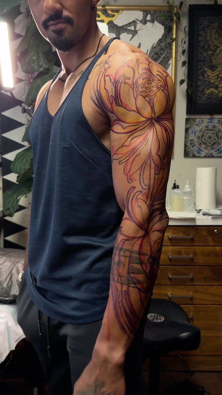 Lotus flower tattoo on a man's arm and shoulder in a studio setting