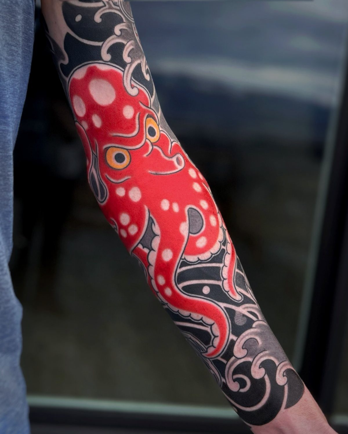 Red octopus tattoo with white spots on an arm with black waves