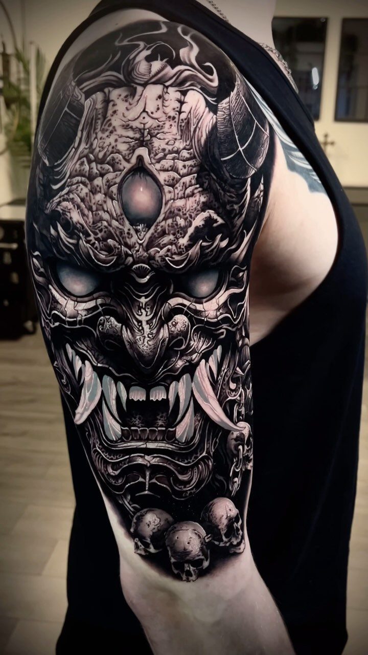 Japanese Oni demon mask tattoo on an upper arm with skulls and horns.