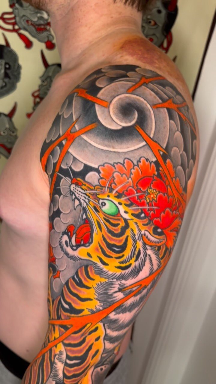 Japanese tiger tattoo on an arm with red flowers and grey clouds