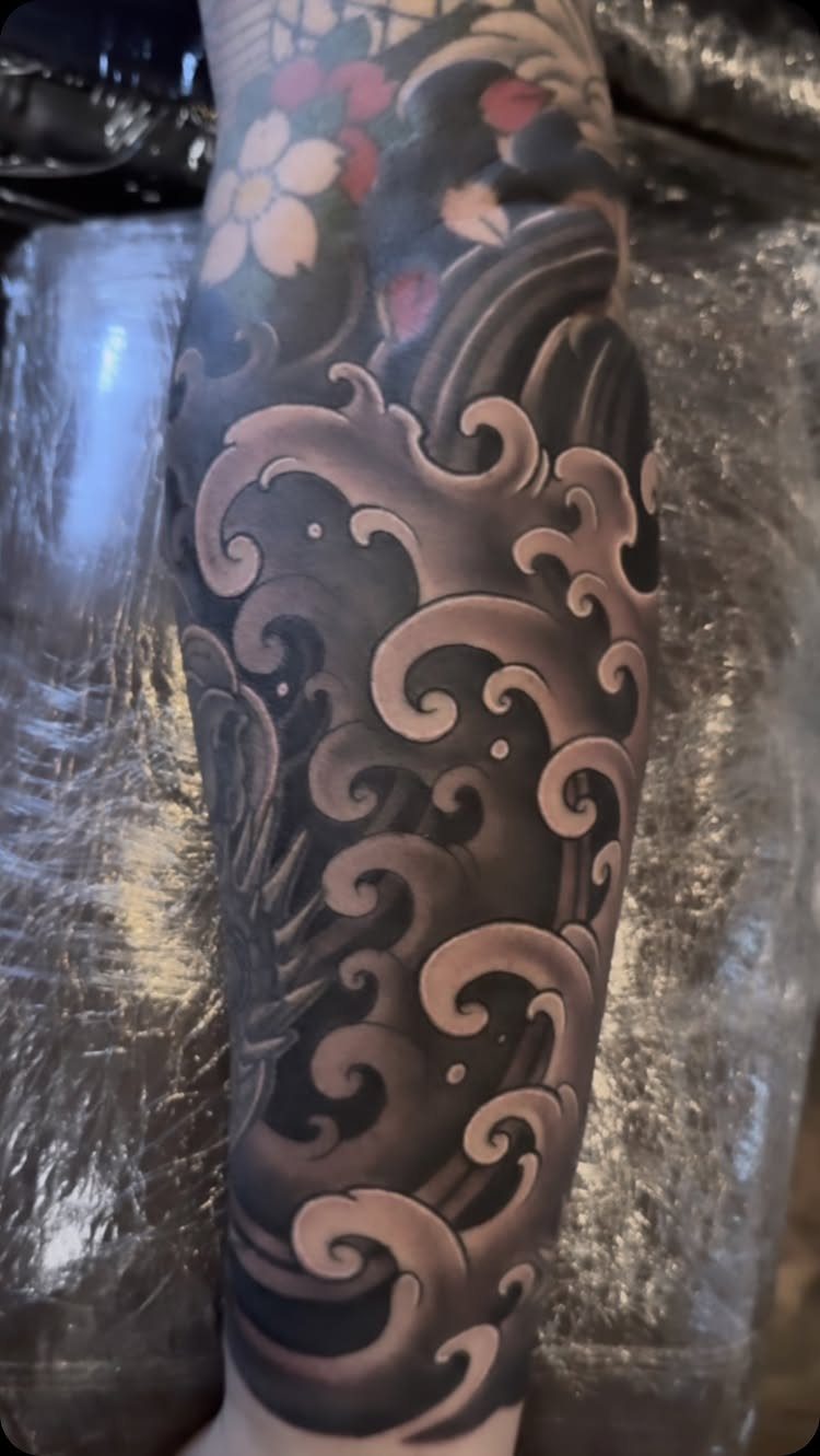 Japanese wave tattoo on an arm with pink cherry blossoms and grey shading