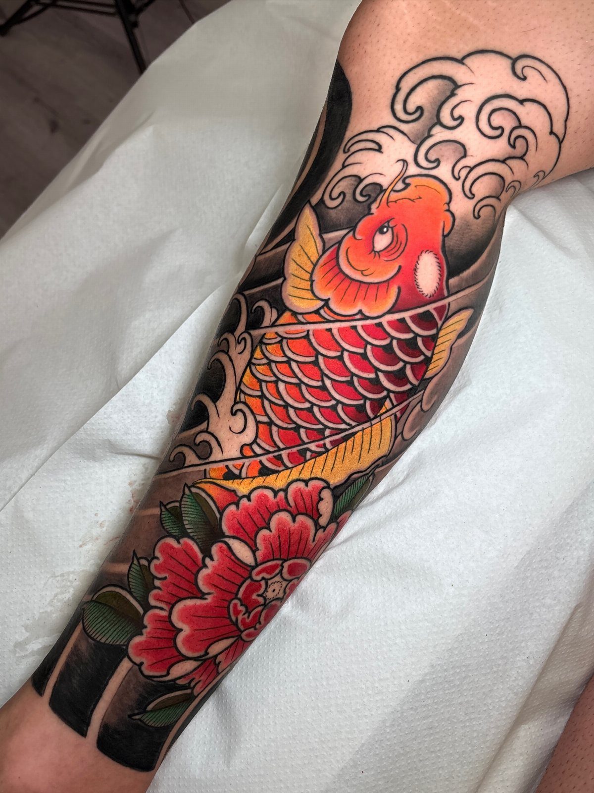 Orange koi fish tattoo with red peony and waves on a human arm