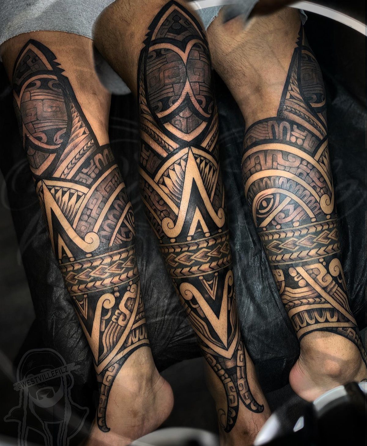 Lower legs with intricate black ink Aztec pattern tattoos covering the calves and ankles.