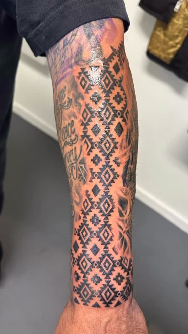 Forearm tattoo featuring a black geometric Aztec pattern with repeating diamond shapes.