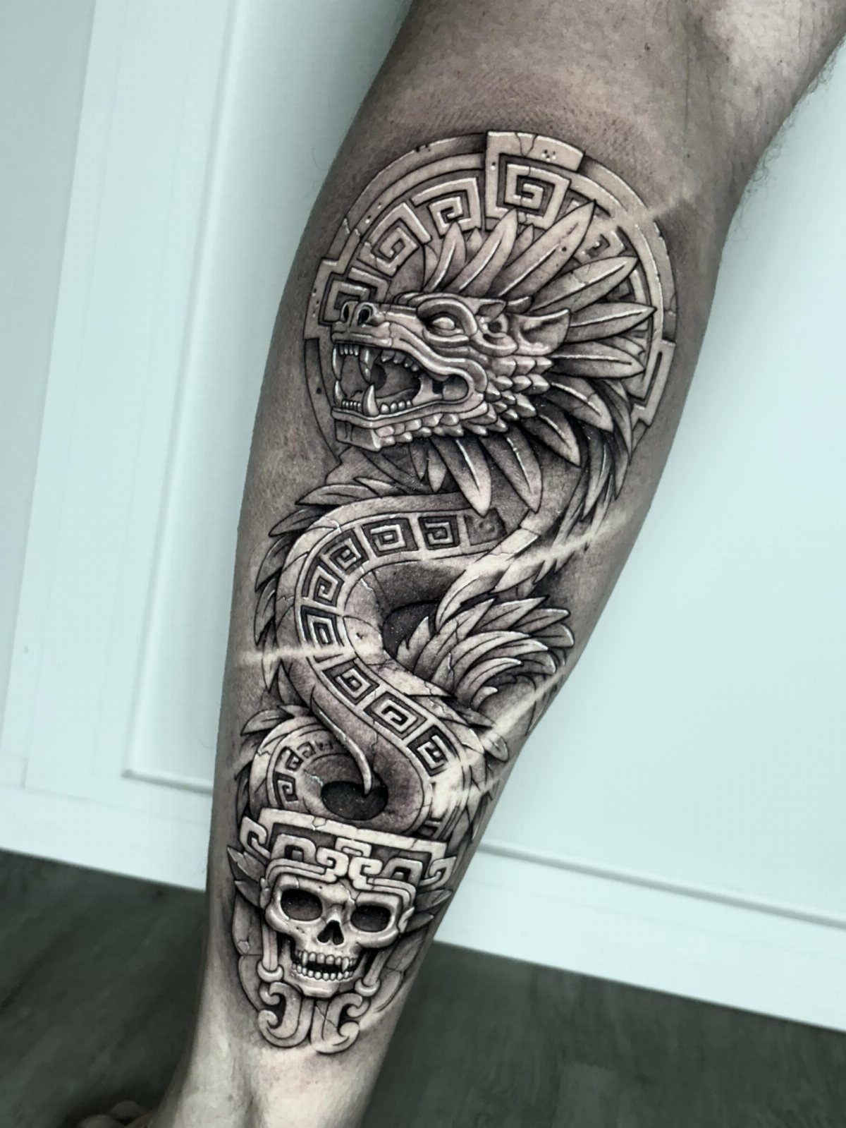 Aztec serpent tattoo with geometric patterns and a skull on a person's leg
