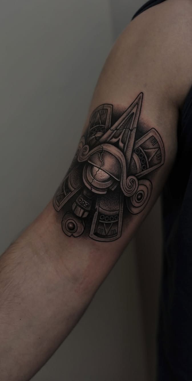 Aztec sun tattoo in black and grey ink on a person's upper arm.