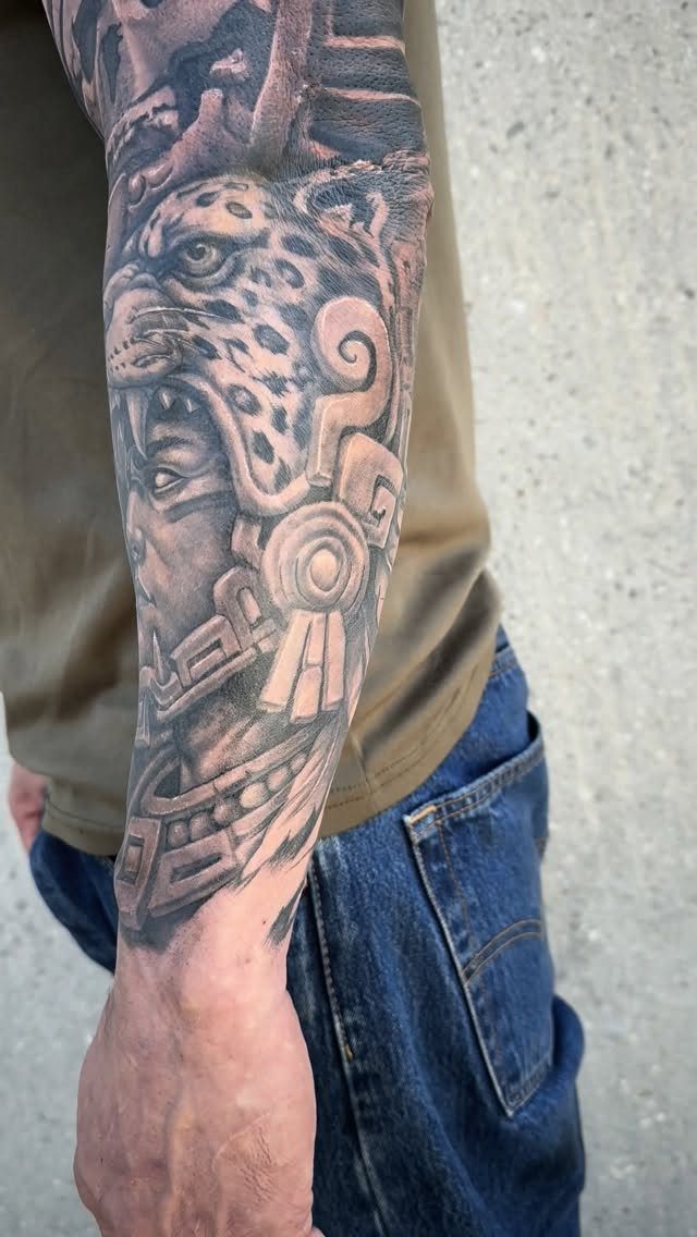 Black and grey Aztec tattoo of a jaguar and warrior on a forearm