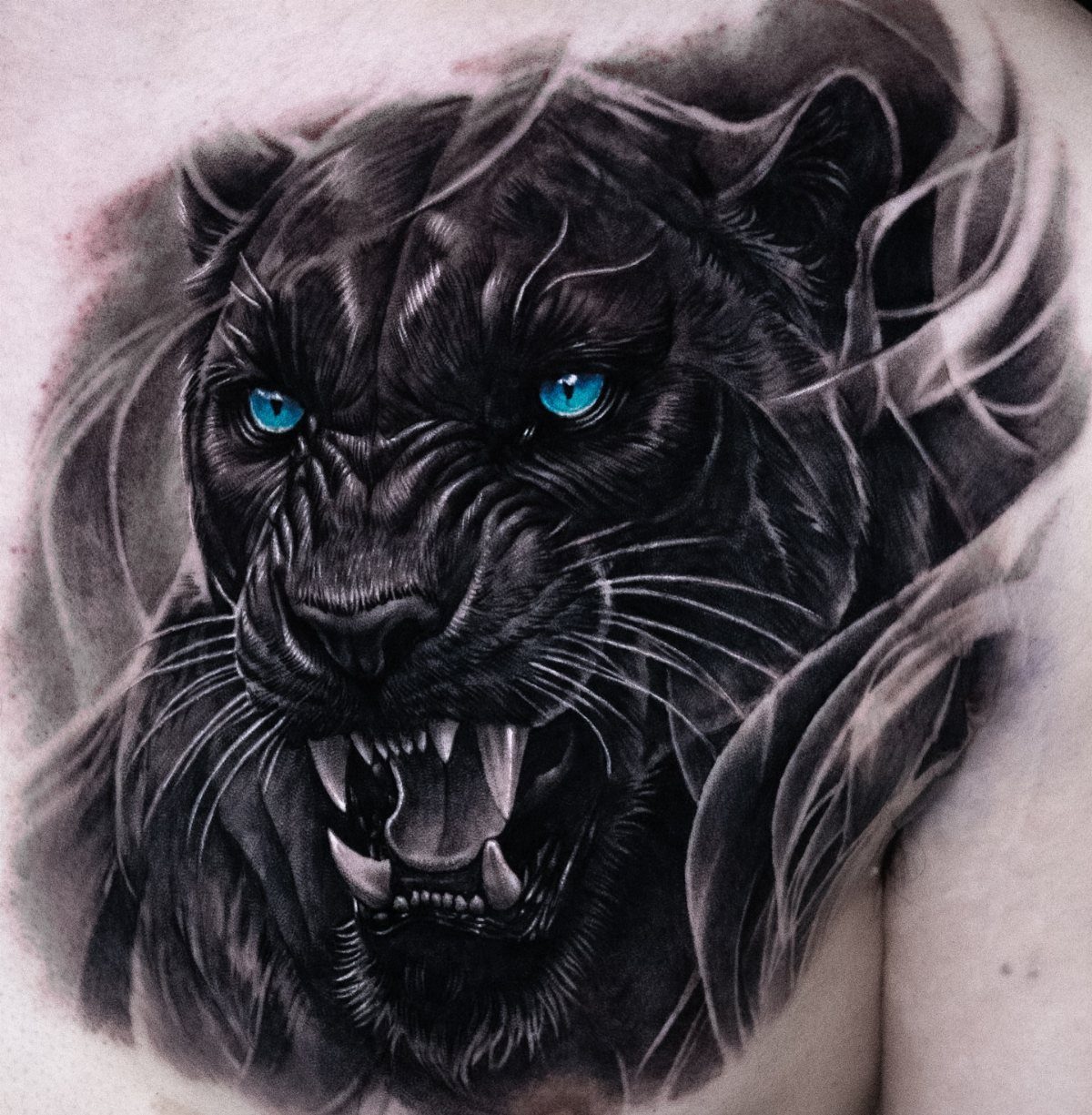 Black panther tattoo with bright blue eyes and snarling mouth on skin